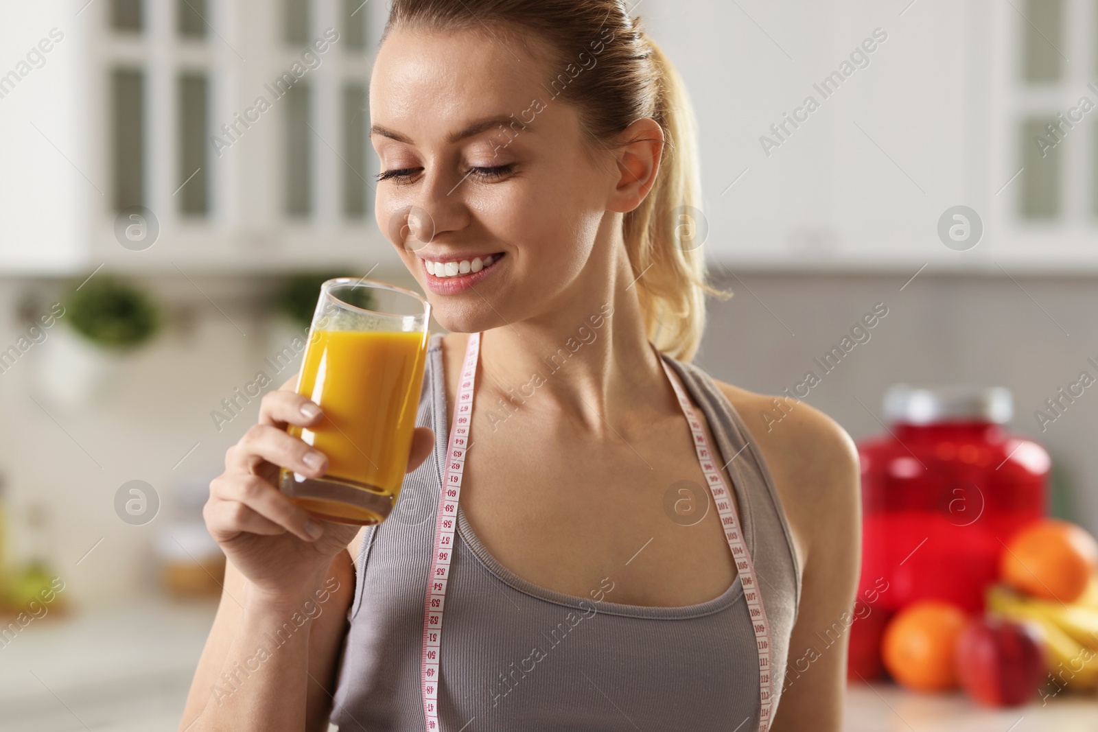 Photo of Weight loss. Happy woman with tasty shake and measuring tape in kitchen