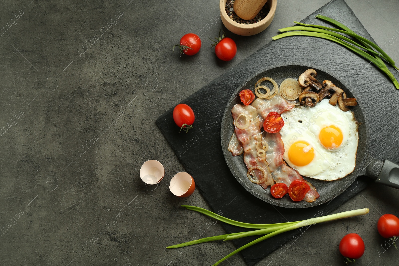 Photo of Tasty fried eggs, bacon and mushrooms served on grey table, flat lay. Space for text