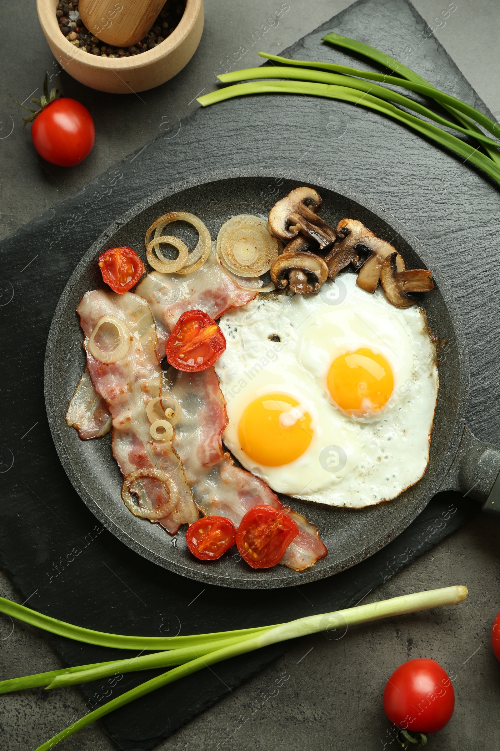 Photo of Tasty fried eggs, bacon and mushrooms served on grey table, flat lay