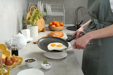 Photo of Woman putting tasty fried eggs onto plate from frying pan in kitchen, closeup