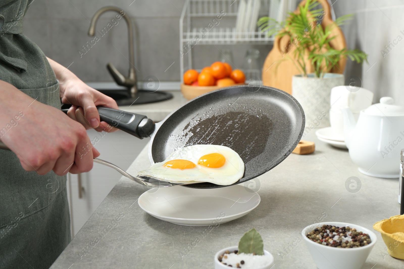 Photo of Woman putting tasty fried eggs onto plate from frying pan in kitchen, closeup