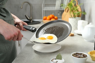 Photo of Woman putting tasty fried eggs onto plate from frying pan in kitchen, closeup