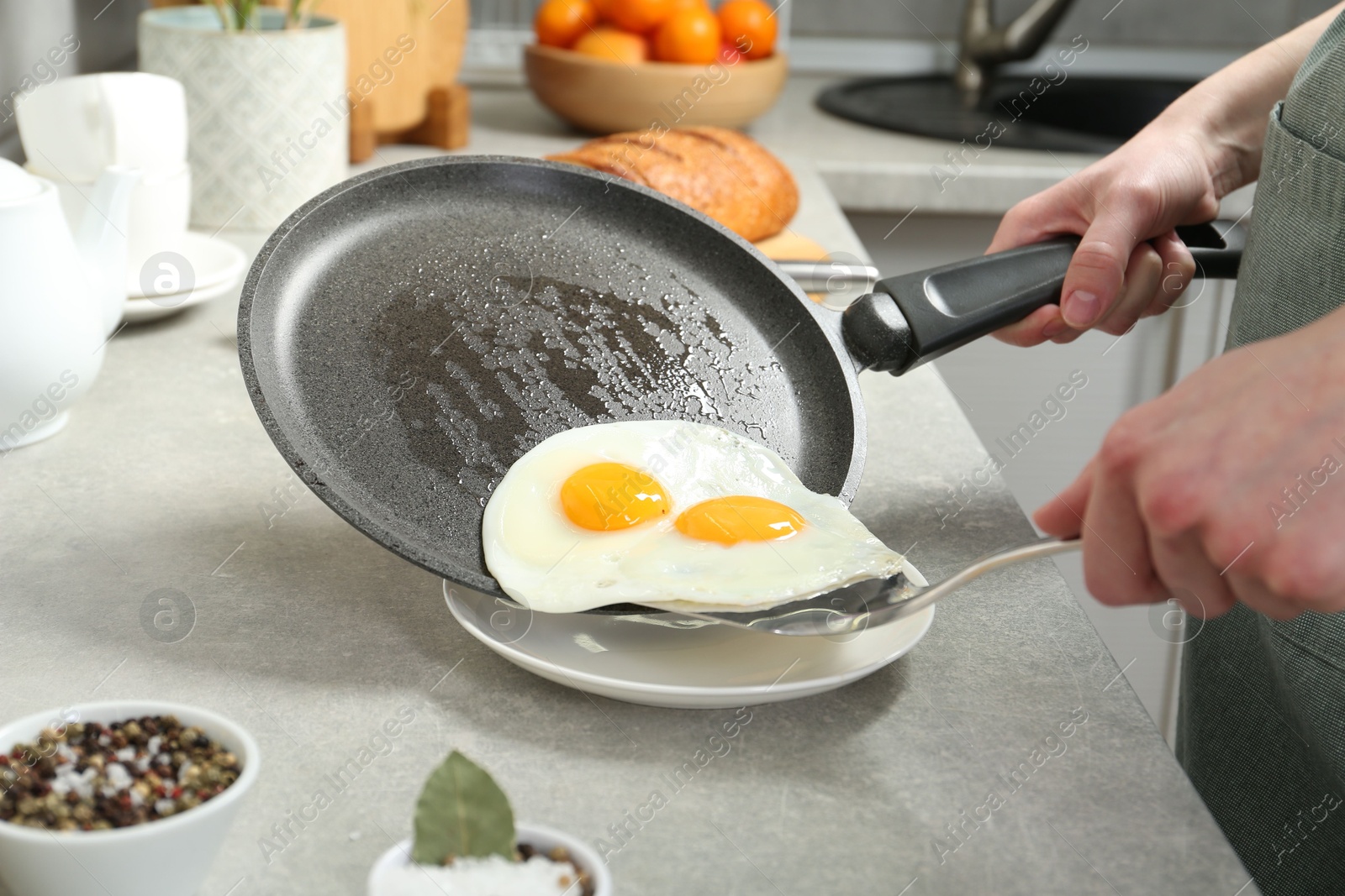 Photo of Woman putting tasty fried eggs onto plate from frying pan in kitchen, closeup