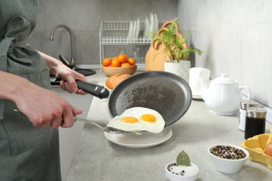 Photo of Woman putting tasty fried eggs onto plate from frying pan in kitchen, closeup