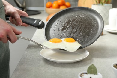 Photo of Woman putting tasty fried eggs onto plate from frying pan in kitchen, closeup