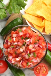 Delicious salsa in bowl, nacho chips and ingredients on white table, flat lay