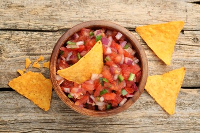 Delicious salsa in bowl and nacho chips on wooden table, flat lay