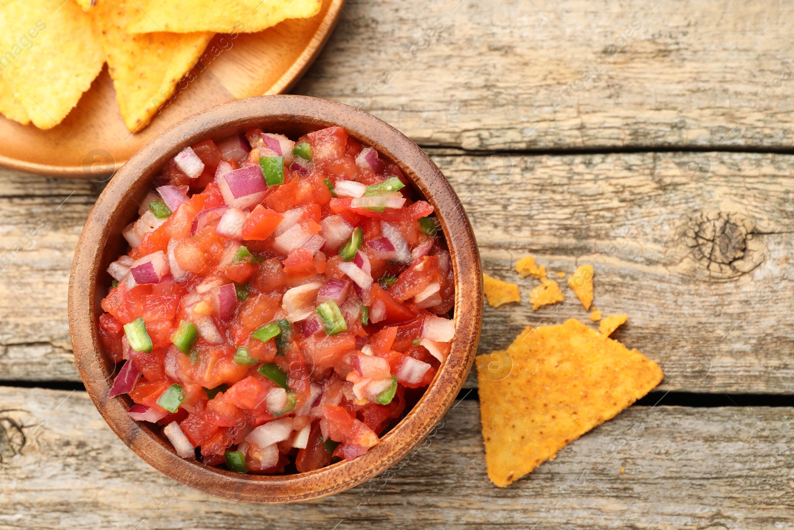 Photo of Delicious salsa in bowl and nacho chips on wooden table, flat lay