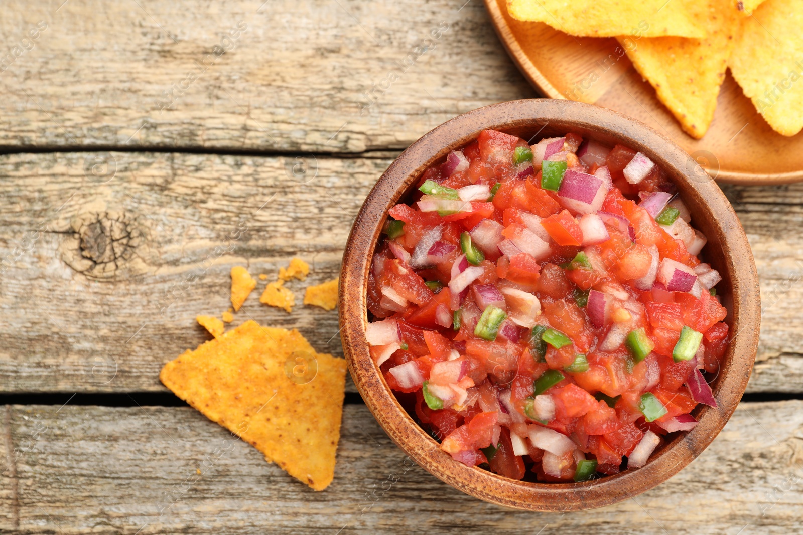 Photo of Delicious salsa in bowl and nacho chips on wooden table, flat lay. Space for text