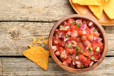 Photo of Delicious salsa in bowl and nacho chips on wooden table, flat lay. Space for text