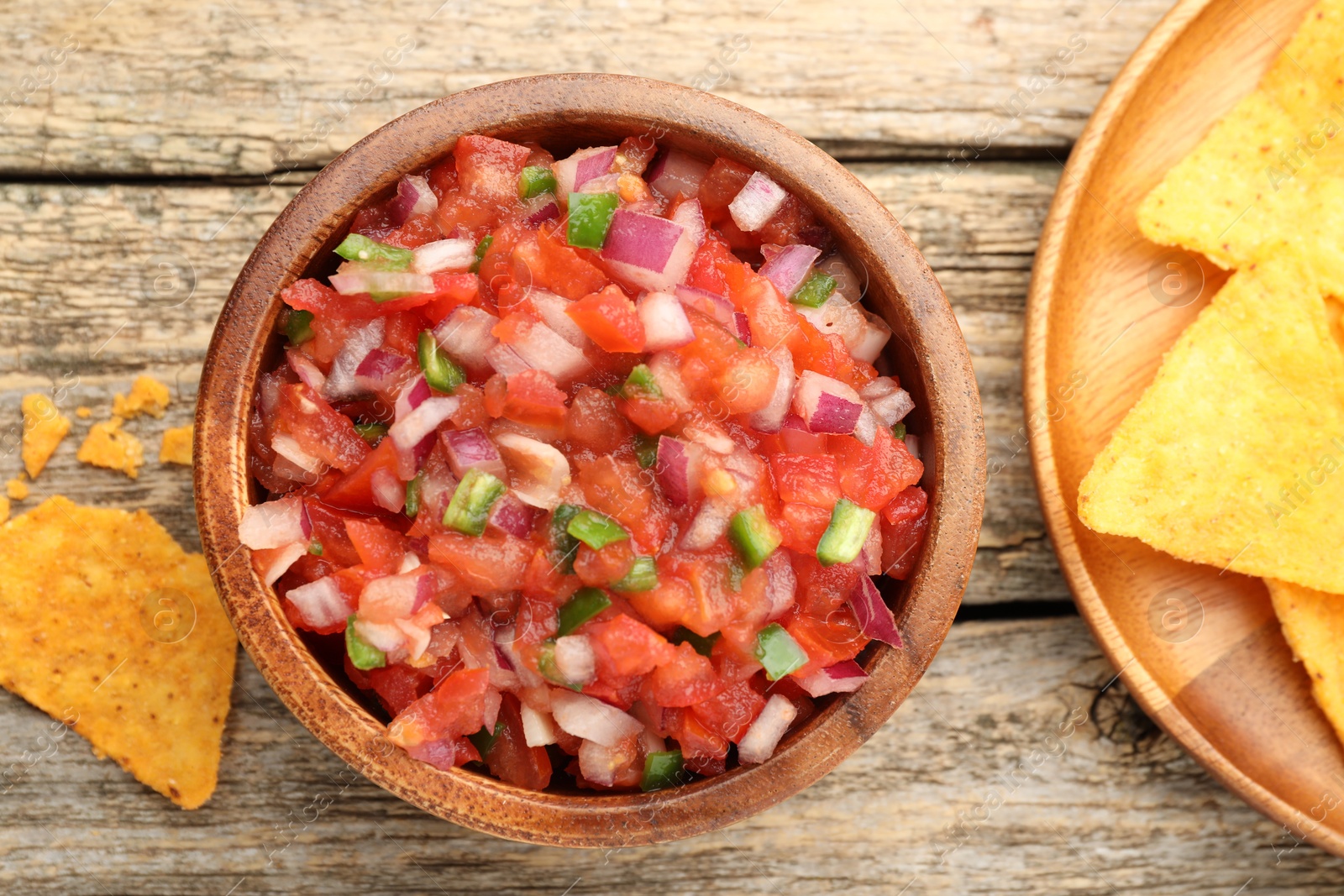 Photo of Delicious salsa in bowl and nacho chips on wooden table, flat lay