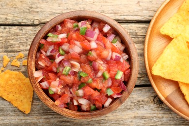 Delicious salsa in bowl and nacho chips on wooden table, flat lay