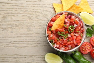 Delicious salsa in bowl, nacho chips and ingredients on wooden table, flat lay. Space for text