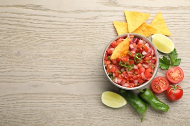 Photo of Delicious salsa in bowl, nacho chips and ingredients on wooden table, flat lay. Space for text