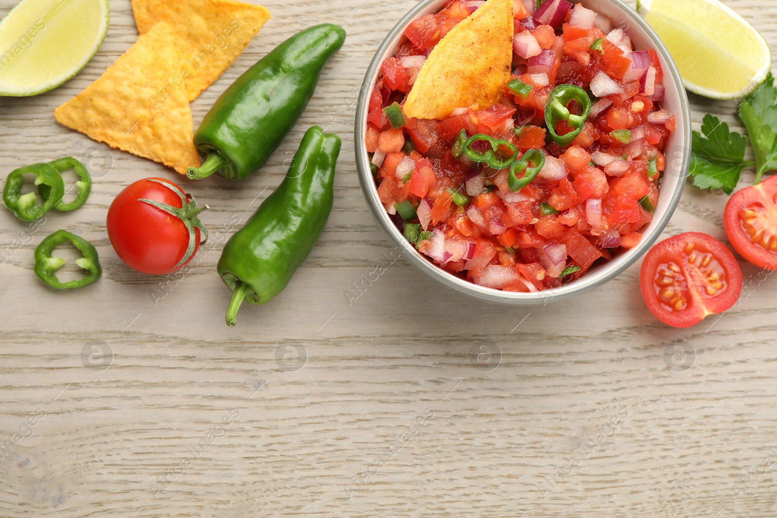 Photo of Delicious salsa in bowl, nacho chips and ingredients on wooden table, flat lay. Space for text