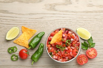 Delicious salsa in bowl, nacho chips and ingredients on wooden table, flat lay. Space for text