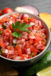 Photo of Delicious salsa in bowl and ingredients on grey table, closeup