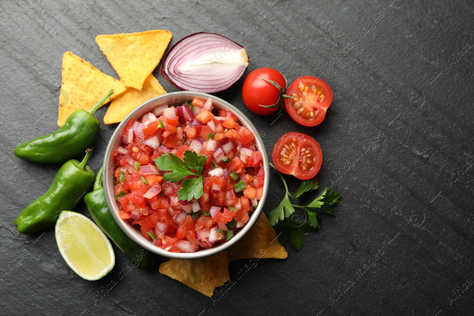 Photo of Delicious salsa in bowl, nacho chips and ingredients on grey table, flat lay