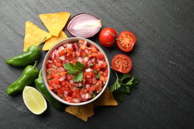 Delicious salsa in bowl, nacho chips and ingredients on grey table, flat lay