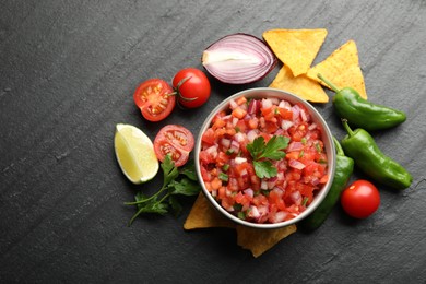 Delicious salsa in bowl, nacho chips and ingredients on grey table, flat lay