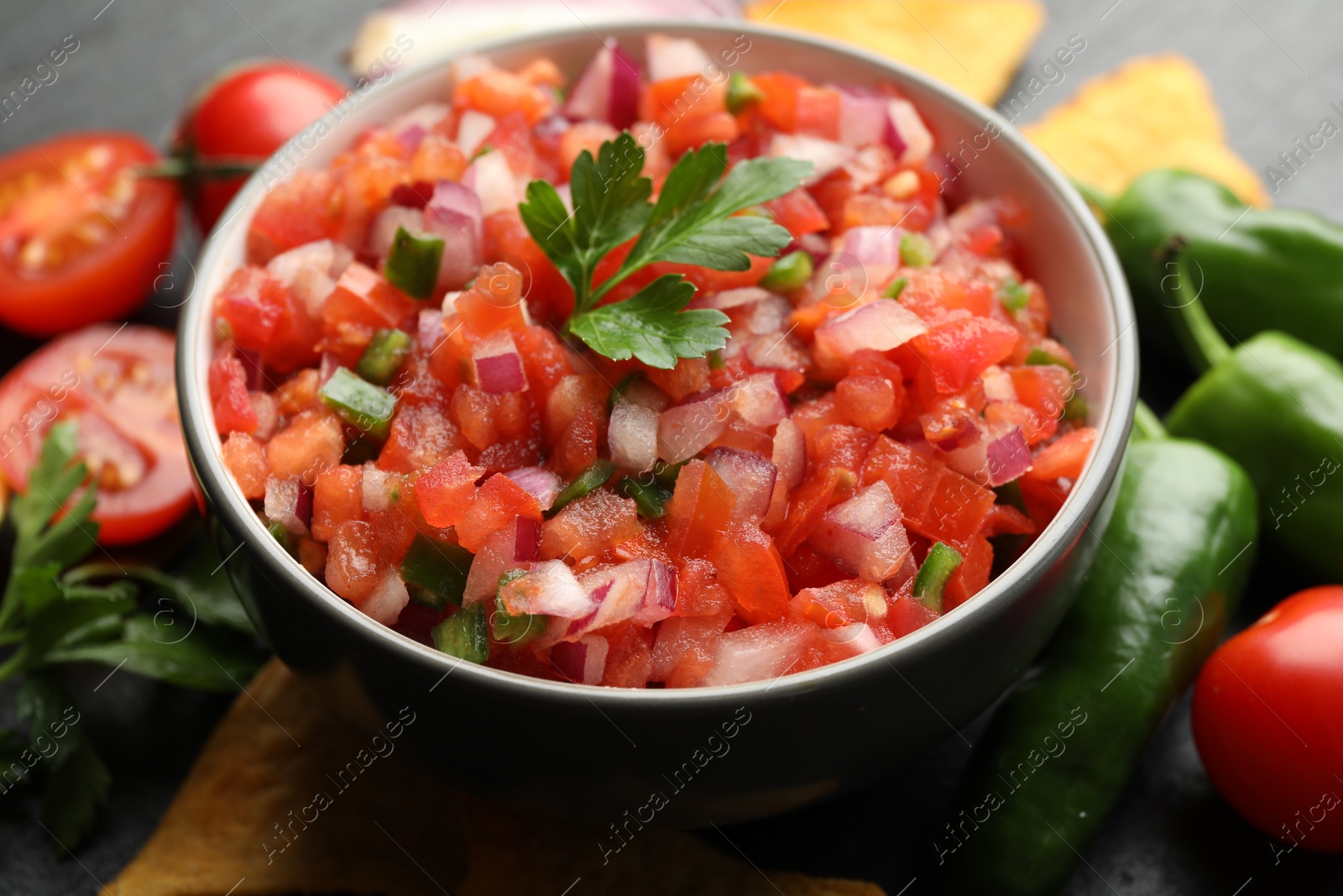 Photo of Delicious salsa in bowl and ingredients on grey table, closeup