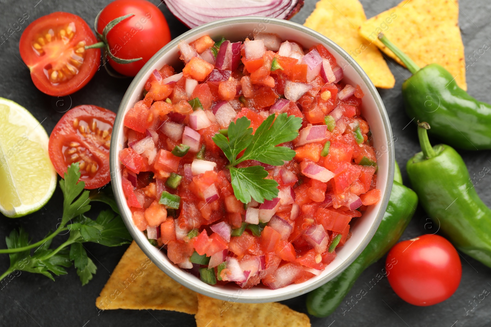 Photo of Delicious salsa in bowl, nacho chips and ingredients on grey table, flat lay