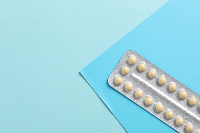 Photo of Blister of contraceptive pills on light blue background, top view. Space for text