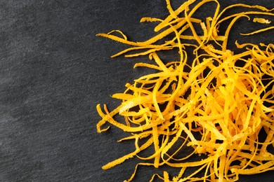 Photo of Pile of fresh orange zest on black table, top view. Space for text