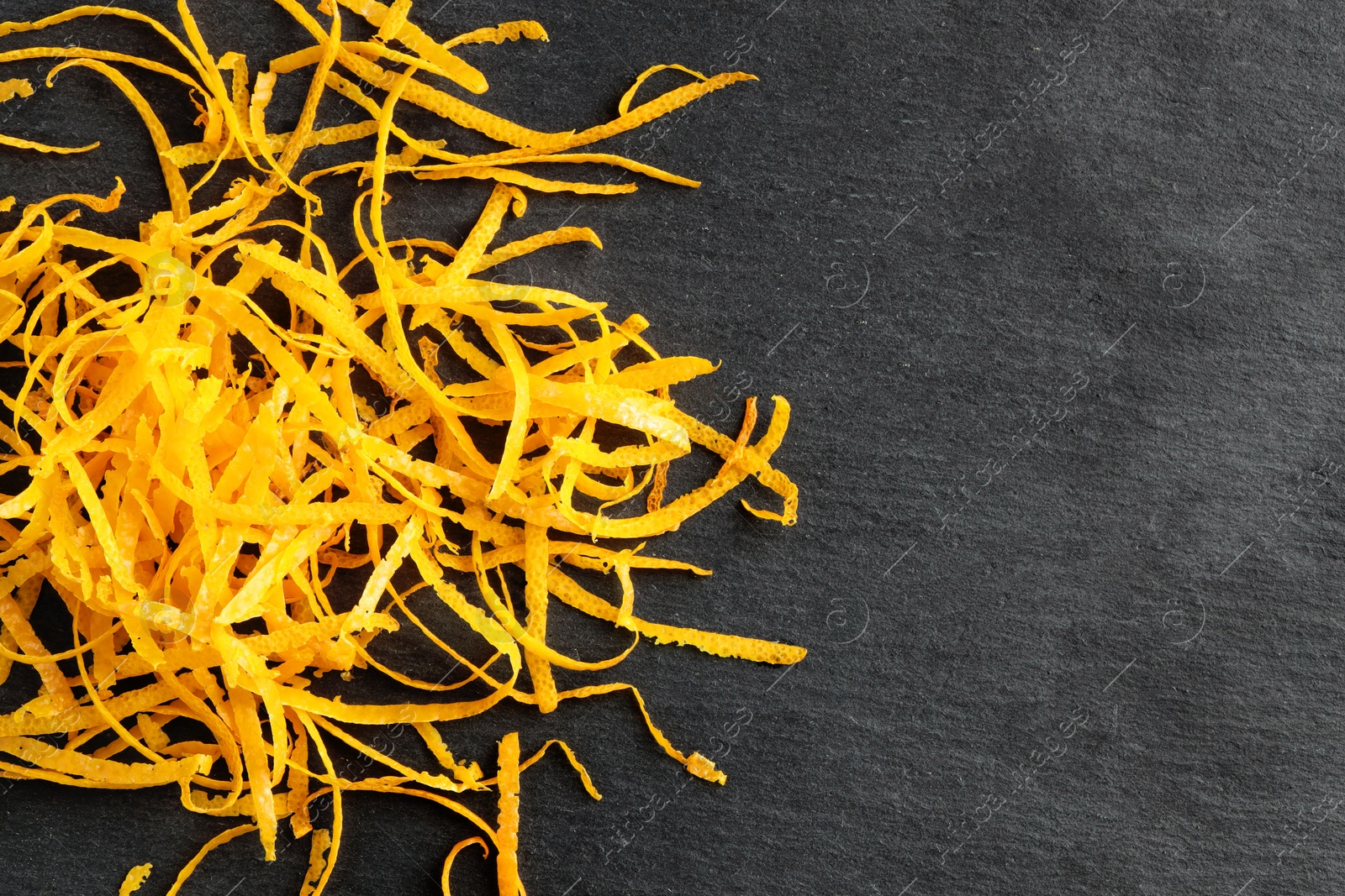 Photo of Pile of fresh orange zest on black table, top view. Space for text