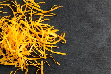 Photo of Pile of fresh orange zest on black table, top view. Space for text