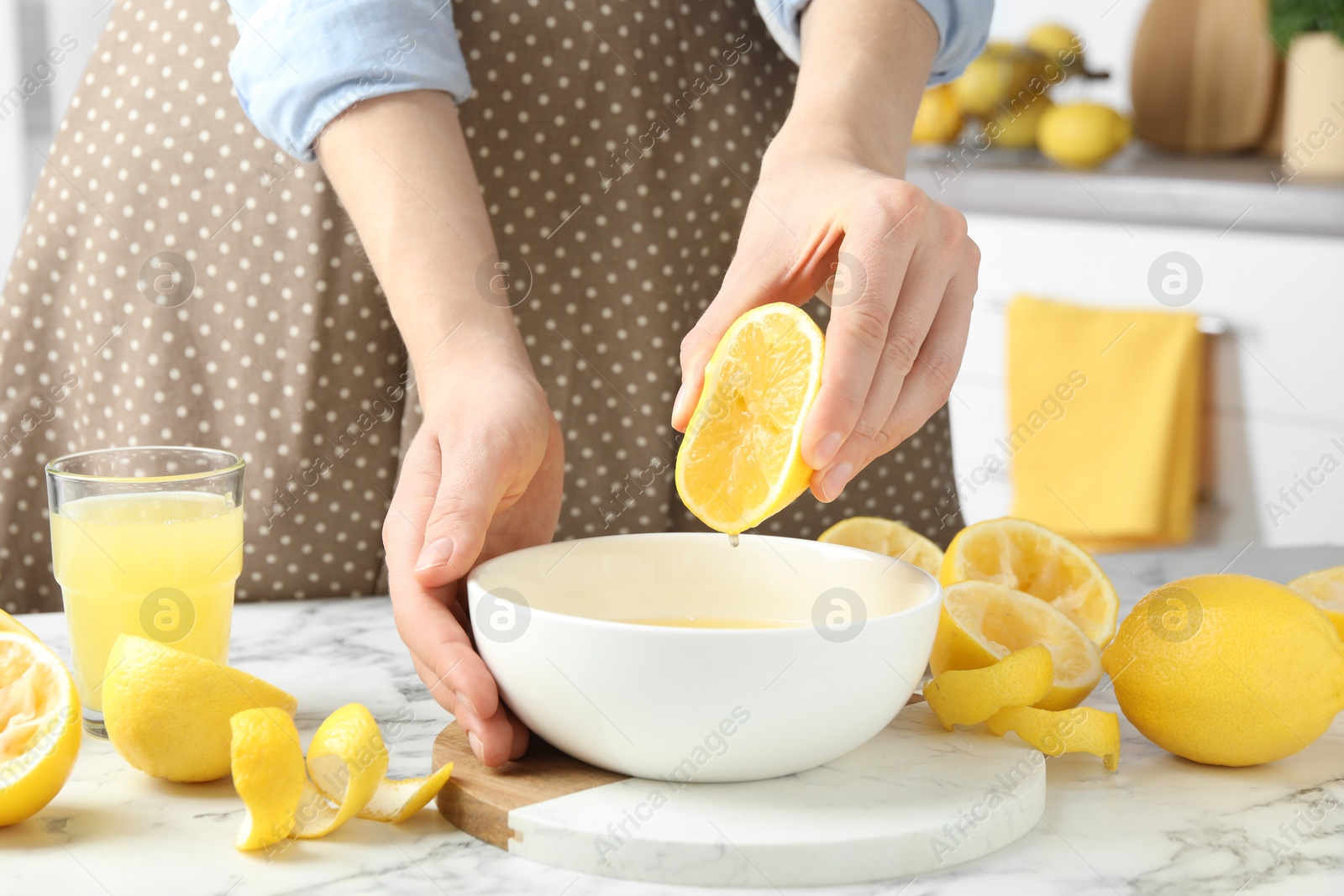 Photo of Woman squeezing lemon juice into bowl at marble table, closeup