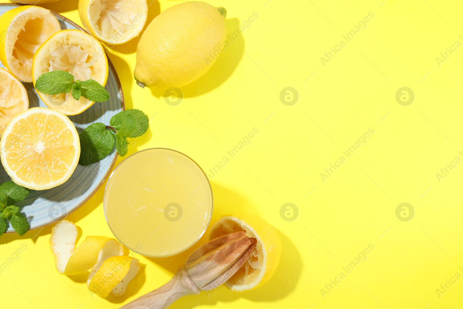 Photo of Glass of fresh lemon juice, squeezer and fruits on yellow background, flat lay. Space for text