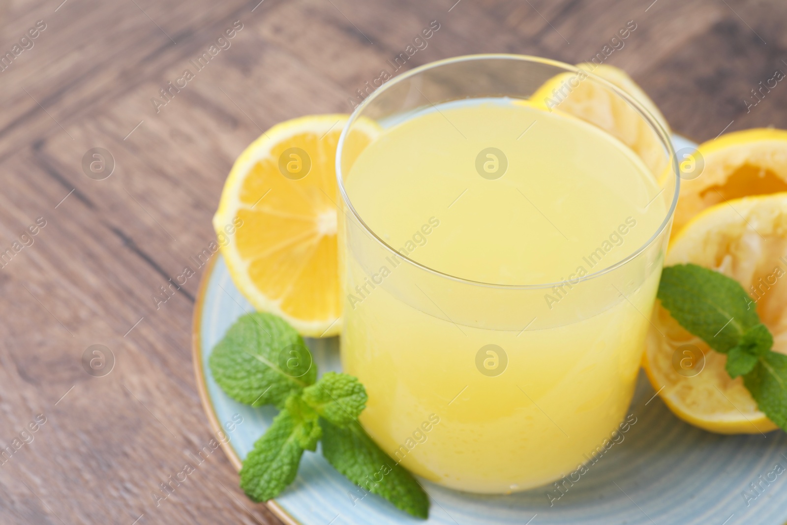 Photo of Glass of lemon juice and fresh fruits on wooden table, closeup