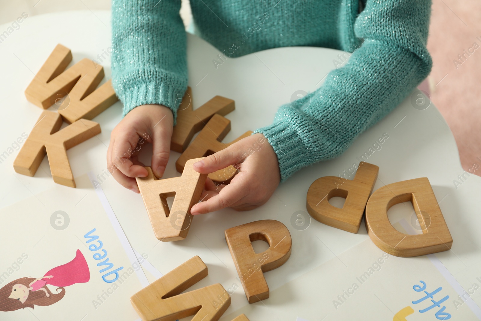 Photo of Little girl learning alphabet with wooden letters at white table indoors, closeup