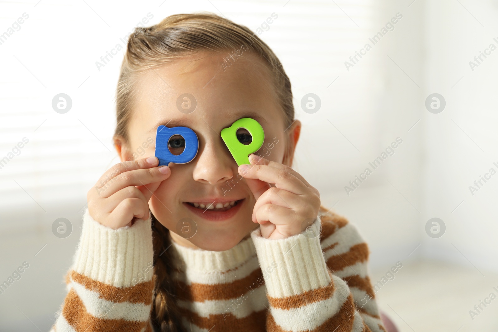 Photo of Learning alphabet. Little girl closing eyes with magnetic letters P indoors