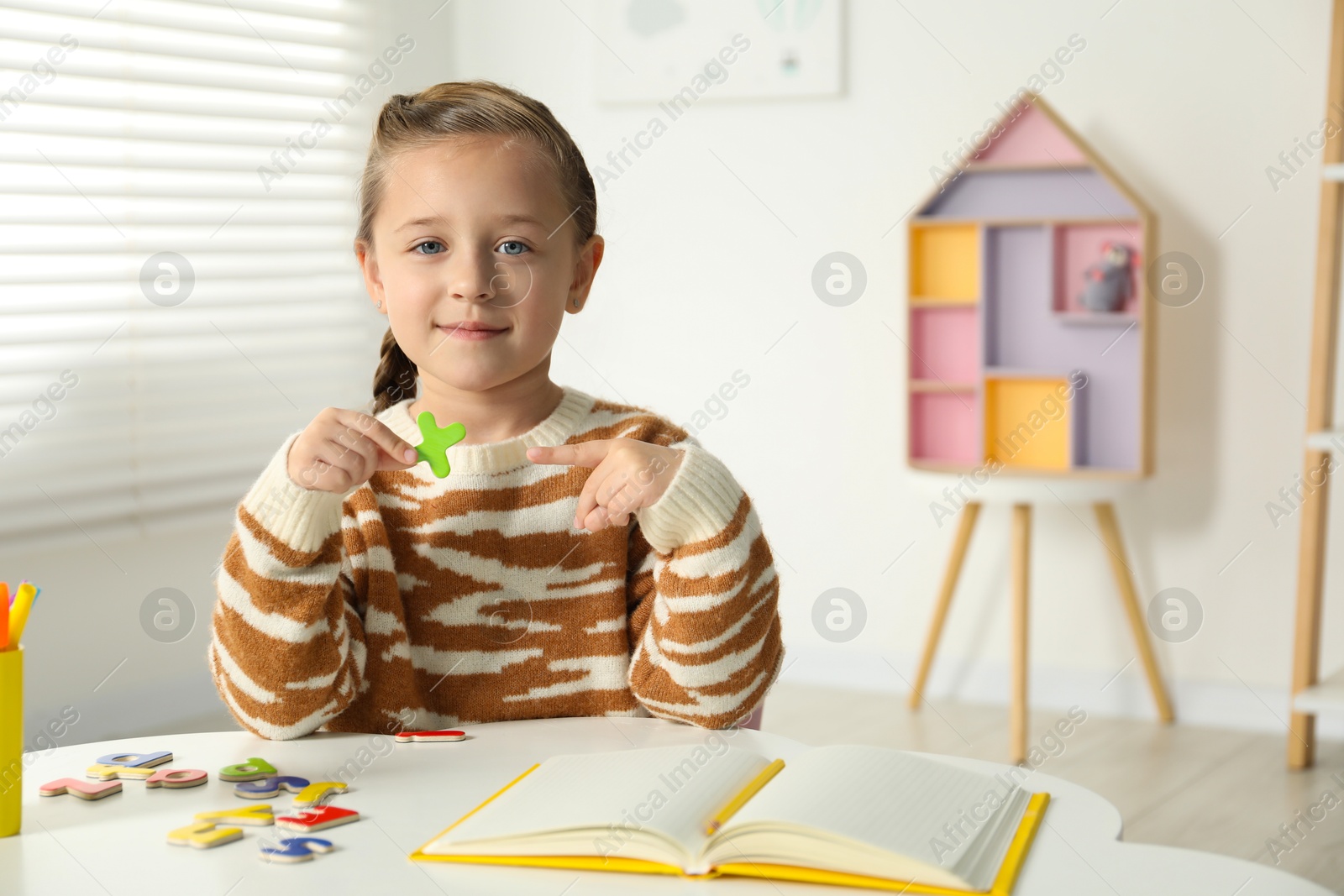 Photo of Little girl learning alphabet with magnetic letters at white table indoors