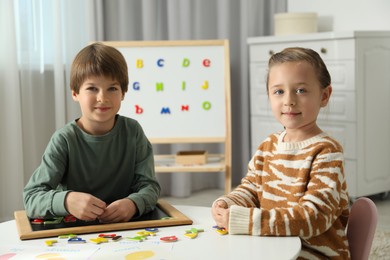 Photo of Little kids learning alphabet with magnetic letters at white table indoors