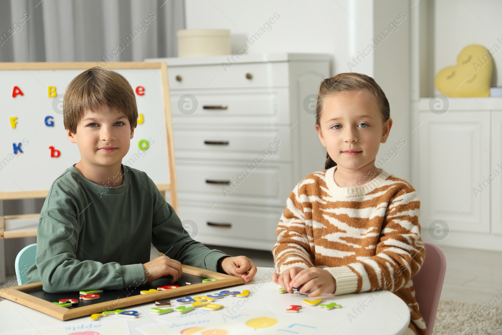 Photo of Little kids learning alphabet with magnetic letters at white table indoors