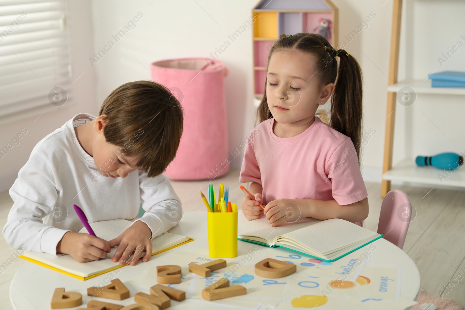 Photo of Little kids learning alphabet at white table indoors