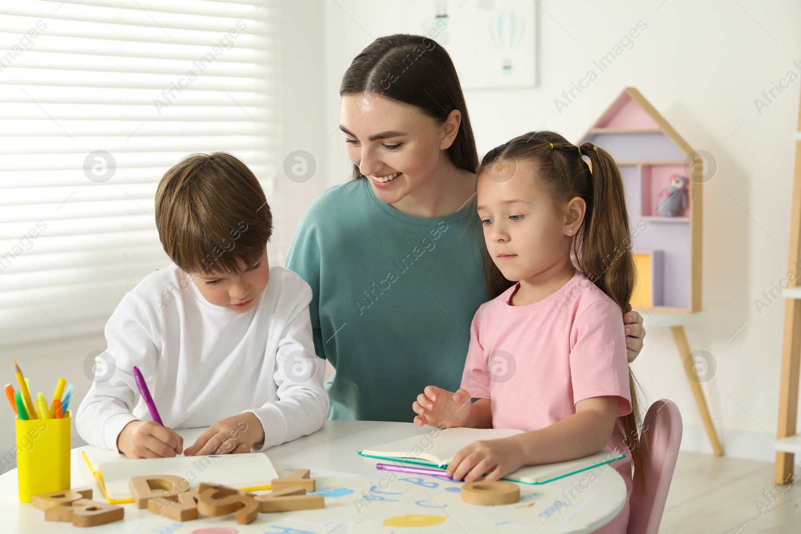 Photo of Speech therapist teaching little kids alphabet at white table indoors