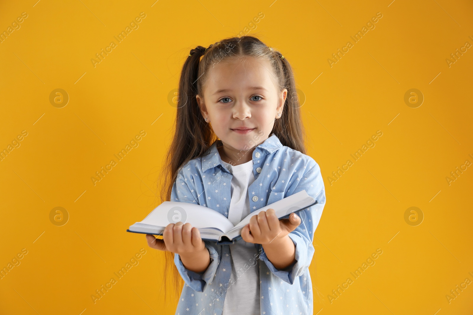 Photo of Learning alphabet. Little girl with book on orange background