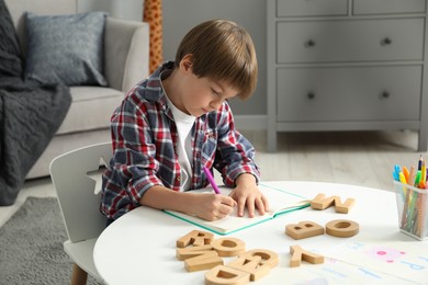 Photo of Little boy learning alphabet at white table indoors