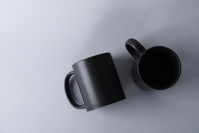 Photo of Two blank black mugs on light background, top view. Mockup for design