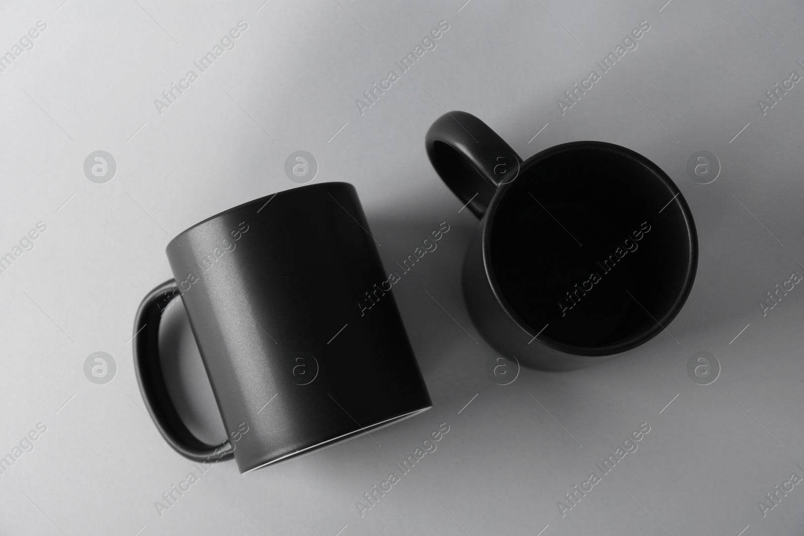 Photo of Two blank black mugs on light background, top view. Mockup for design