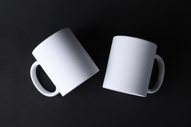 Photo of Two blank white mugs on black background, top view. Mockup for design