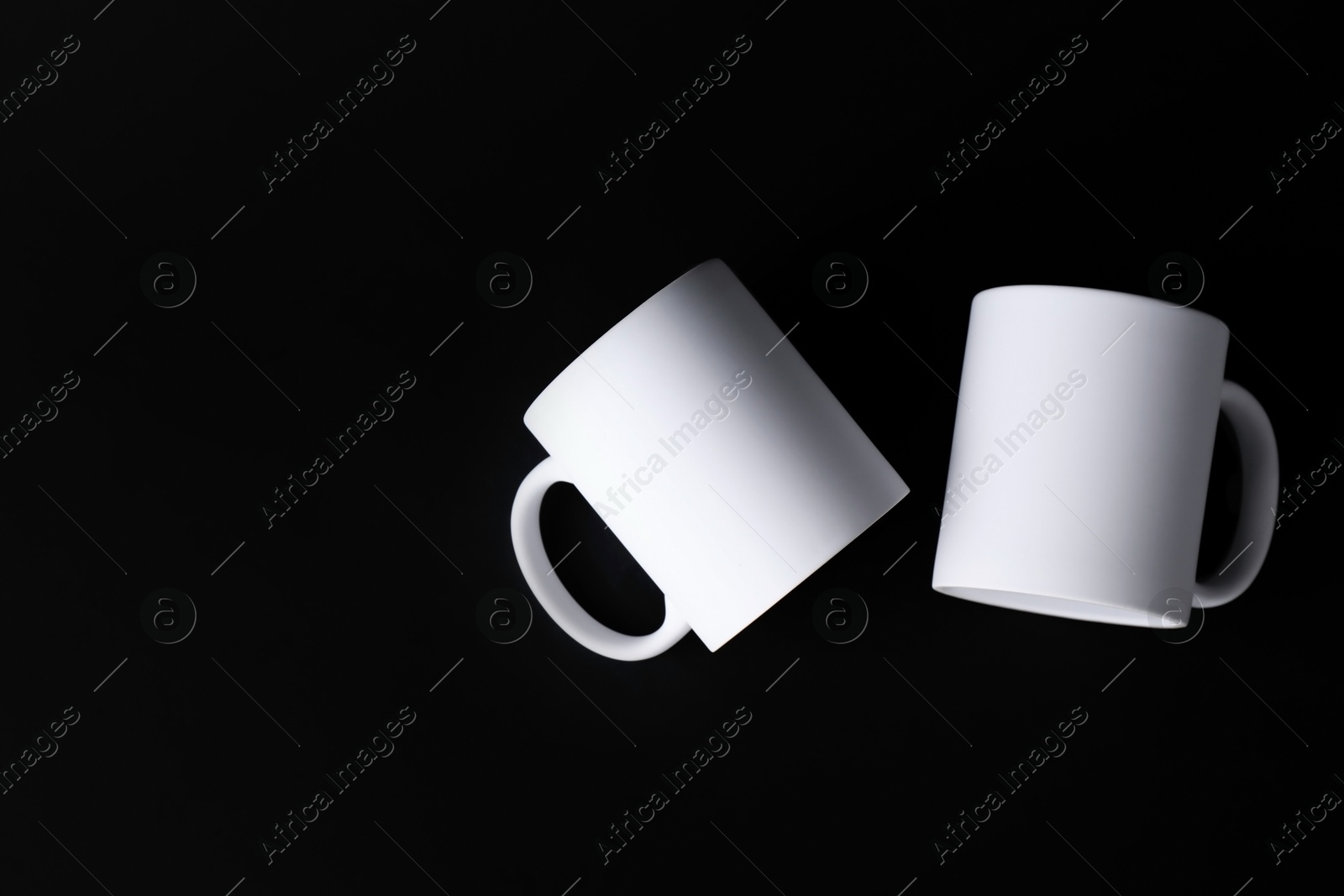 Photo of Two blank white mugs on black background, top view. Mockup for design