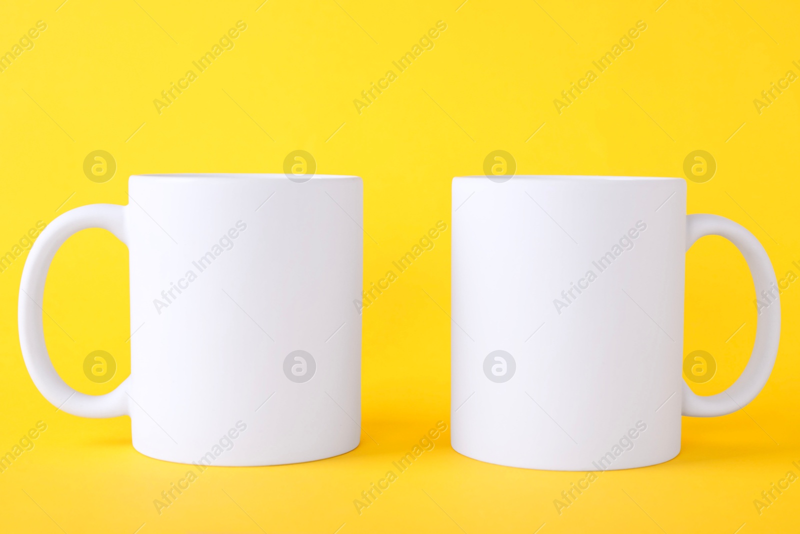 Photo of Two blank white mugs on yellow background. Mockup for design