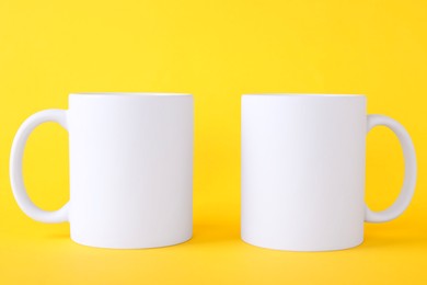 Photo of Two blank white mugs on yellow background. Mockup for design