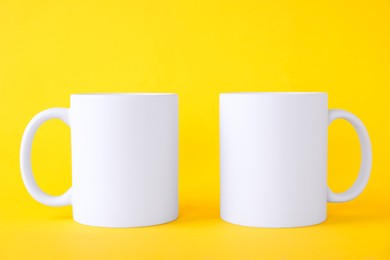 Photo of Two blank white mugs on yellow background. Mockup for design