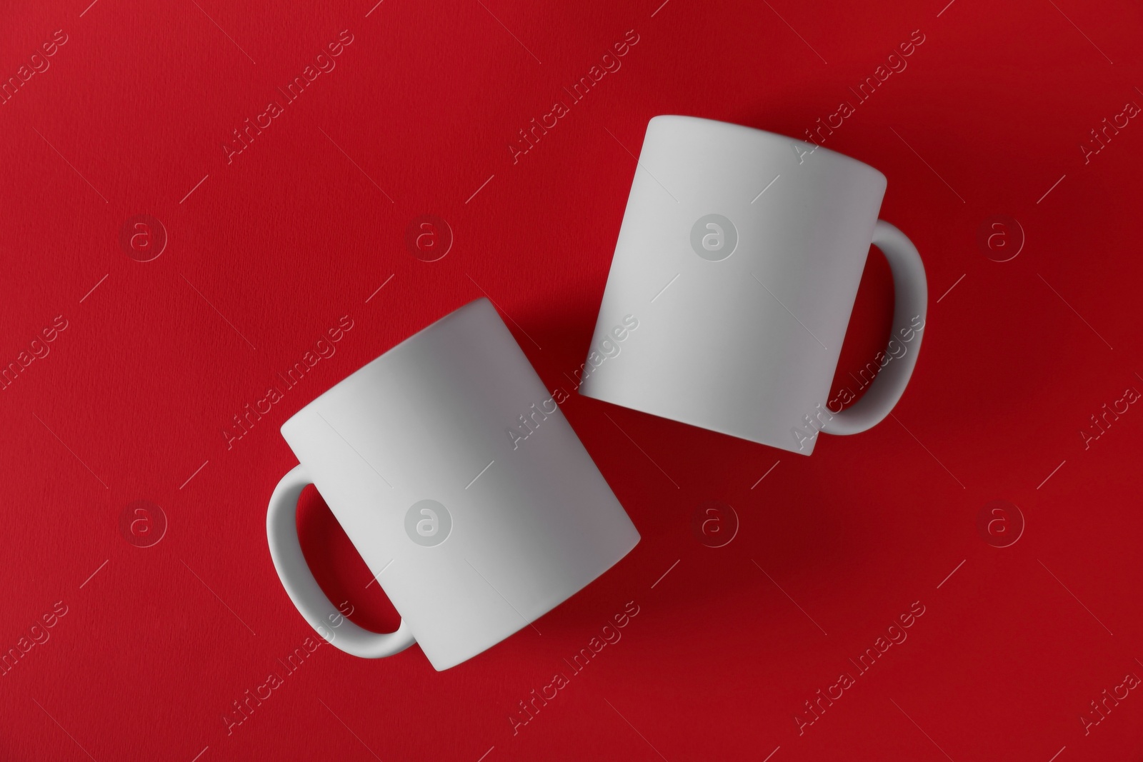 Photo of Two blank white mugs on red background, top view. Mockup for design